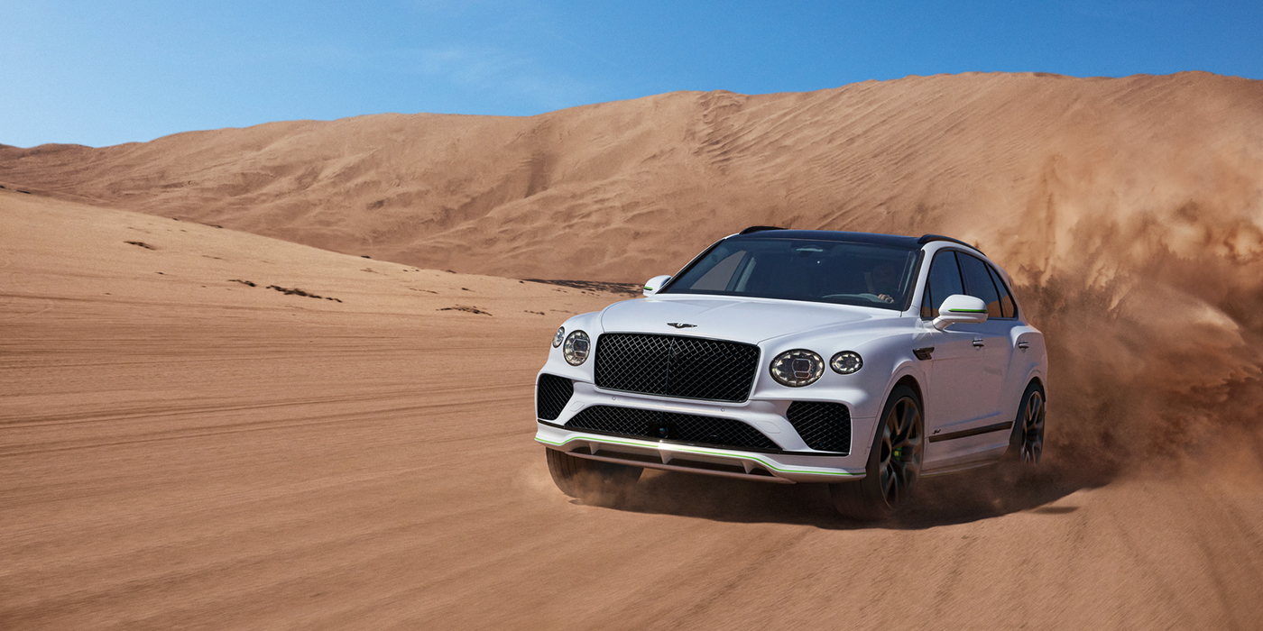 Bentley Jeddah Bentley Bentayga Speed SUV front three quarter in Snow Quarts Pearlescent by Mulliner white paint driving dynamically through the desert