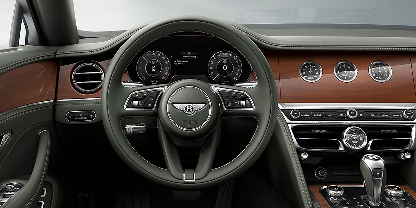 Bentley Jeddah New Bentley Flying Spur sedan front cabin in Cumbrian Green hide and Crown Cut walnut veneer showing steering wheel and Rotating Display with three clocks on face