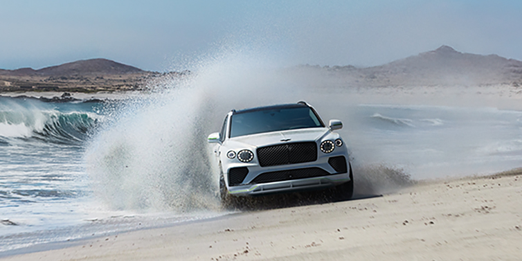 Bentley Jeddah Bentley Bentayga Speed SUV facing front in Snow Quarts Pearlescent white paint driving dynamically on beach