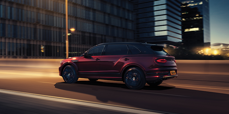 Bentley Jeddah Bentley Bentayga Extended Wheelbase Mulliner SUV in Cricket Ball red paint driving dynamically in city at night