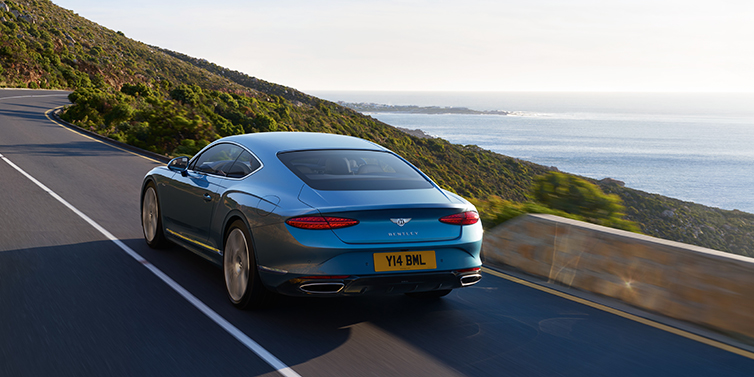 Bentley Jeddah New Bentley Continental GT Azure coupe in Light Windsor blue paint seen from the rear driving dynamically on a seaside road